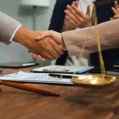 Uścisk dłoni prawników przy biurku z młotkiem sędziowskim i wagą sprawiedliwości. Zastanawiasz się, ile zarabia sędzia?