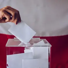 Dłoń wrzuca kartę do urny wyborczej. To ważny moment kampanii wyborczej, gdzie każdy głos ma znaczenie.