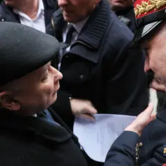 Straż marszałkowska w mundurach rozmawia z mężczyzną w czarnym berencie. Jeden z funkcjonariuszy pokazuje dokument.