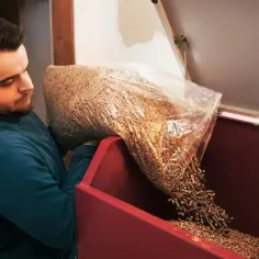 Mężczyzna wsypuje pellet z worka do czerwonego zasobnika.