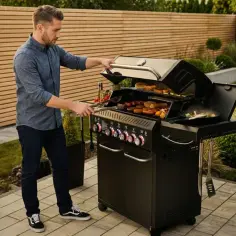 Mężczyzna przygotowuje jedzenie na grillu gazowym. Widać kiełbaski, bułki i warzywa. To idealne części do grilla gazowego na letnie spotkania.