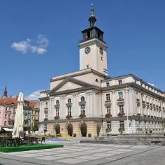 Słoneczny rynek w Kaliszu z ratuszem i wieżą zegarową. Stoliki kawiarniane czekają na gości.