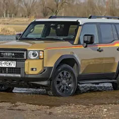 Złoty Land Cruiser 100 z kolorowymi pasami na boku, stojący w wodzie.