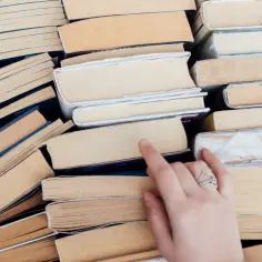 Stos książek, wśród nich lektury klasa 8. Dłoń sięga po jedną z nich, by rozpocząć czytanie.