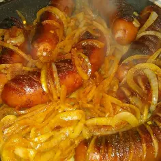 Smażona kiełbasa z cebulą na patelni, parująca i apetyczna.