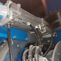Metalowy siłownik pneumatyczny zamontowany na niebieskiej konstrukcji, z przewodami i elementami mechanicznymi.