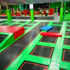 Wielopoziomowy park trampolin z zielonymi i czerwonymi elementami, w tym z podestami i poduszkami.