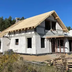 Budowa domu z bloczków, z widocznym szkieletem dachu. To początek realizacji indywidualny projekt domu w otoczeniu lasu.