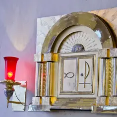 Złote tabernakulum z symbolami ryby i monogramem IHS. Obok pali się czerwona lampka.