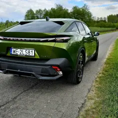 Nowy Peugeot 408 w zielonym kolorze na tle sadu i łąki. Elegancki tył samochodu z charakterystycznymi światłami.