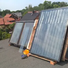 Kolektory słoneczne na dachu, w tle domy i drzewa.