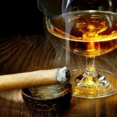 Dymiące cygaro i kieliszek bursztynowej whisky. Czy whisky jest zdrowe? To pytanie pozostaje otwarte, gdy patrzymy na ten obraz.