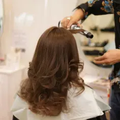 Profesjonalny styling włosów w salonie. Fryzjerka kręci loki na lokówce, tworząc efektowną fryzurę.