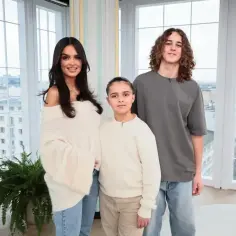 Klaudia El Dursi z dziećmi, synem i córką, pozuje do zdjęcia na tle okna z widokiem na miasto.