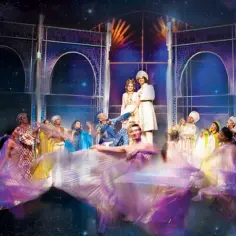 Scena z musicalu "Aladyn" w teatrze w Warszawie. Tancerze w barwnych strojach i księżniczka z księciem na scenie.