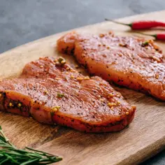 Dwa kawałki indyka w marynacie z gorczycą i pieprzem, obok gałązka rozmarynu i dwa czerwone chili.