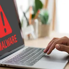 Czerwony wykrzyknik i napis "MALWARE" na ekranie laptopa, ostrzegający przed zagrożeniem, takim jak spyware.