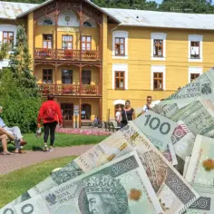Sanatoria nad morzem: czy stać nas na zdrowie? Złotówki w tle żółtego budynku i wypoczywających ludzi.