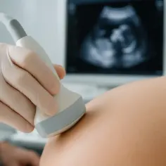 Badania prenatalne: czy na badania prenatalne trzeba być na czczo? Lekarz wykonuje USG brzucha ciężarnej, na ekranie widać obraz płodu.