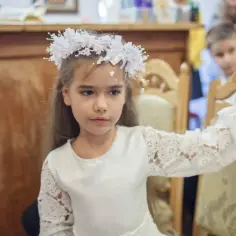 Dziewczynka w białej sukience i wianku na głowie podczas komunii.