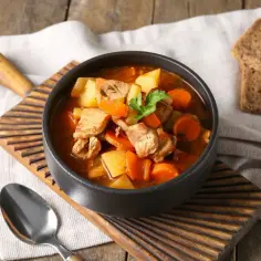 Aromaticzny gulasz z karkówki z ziemniakami i marchewką, podany w misce z chlebem.