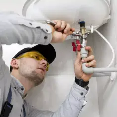 Hydraulik w okularach ochronnych naprawia bojler, używając narzędzi i rur.