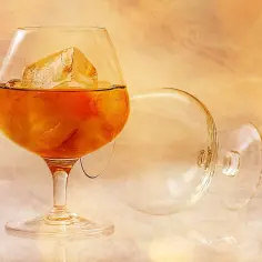 Szklanka z bursztynowym napojem i lodem, obok pusta szklanka. Idealnie, jak pić brandy napoleon.