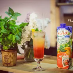 Orzeźwiający drink z sokiem żurawinowym, udekorowany miętą i cytryną, obok karton soku grejpfrutowego.