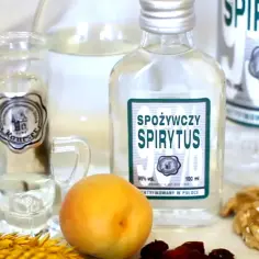Butelki spirytusu, kieliszek, owoce i orzechy. Pokazuje, jak się robi spirytus.