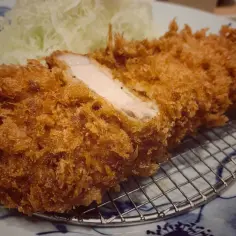Chrupiący kotlet wieprzowy, przekrojony, odsłaniający soczyste mięso, podany z poszatkowaną kapustą i sosem tonkatsu.