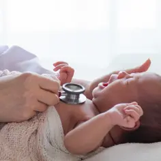 Lekarz osłuchuje noworodka stetoskopem. Wczesne wykrycie chorób metabolicznych, jak fenyloketonuria, jest kluczowe dla zdrowia dziecka.