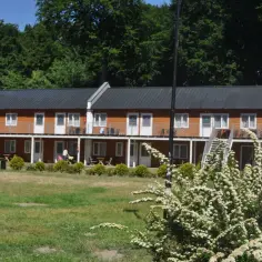 Hotel Stilo w otoczeniu zieleni. Dwa piętra drewnianych domków z balkonami i schodami.