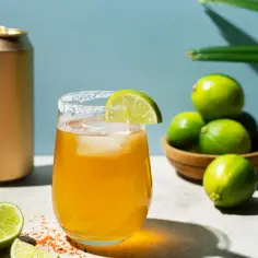 Orzeźwiający drink z Metaxą i colą, udekorowany limonką i solą, obok stoi złota puszka.