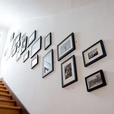 Inspiracja, jak dobrać ramki do domowej galerii zdjęć na klatce schodowej. Różnorodne czarno-białe fotografie w czarnych i białych ramach tworzą galerię.