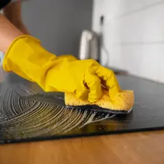Ręka w żółtej rękawiczce czyści płytę indukcyjną gąbką z pianą. Czy mycie płyty indukcyjnej płynem do szyb to dobry pomysł?
