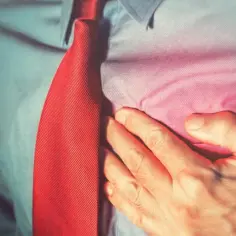 Mężczyzna w czerwonym krawacie trzyma się za serce, odczuwając ból. Może to być sygnał, by zadbać o swoje concor cor.
