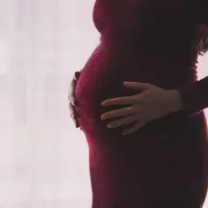 Brzuszek kobiety w czerwonej sukience. Kto płaci macierzyński pracodawca czy ZUS? To pytanie nurtuje wiele przyszłych mam.