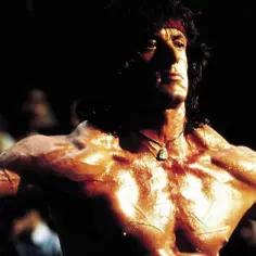 Sylvester Stallone w filmach, muskularny Rambo z czerwoną opaską na czole, błyszczący od potu.