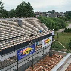 Budowa dachu z widoczną **powłoką antykondensacyjną** i pracownikiem na rusztowaniu.