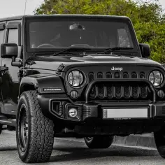 Czarny Jeep Wrangler, idealny SUV do 80 tys. zł, z terenowymi oponami i solidnym grillem, gotowy na przygodę.