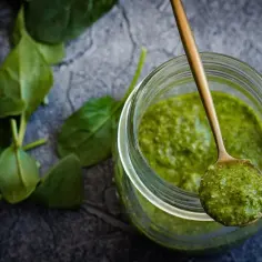 Słoik z zielonym pesto i łyżka z porcją sosu, obok liście szpinaku.