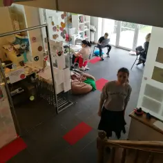 Wnętrze z elementami edukacji alternatywnej: dzieci i młodzież pracują, uczą się, bawią. Widać kolorowe dekoracje, tablice, wygodne siedziska.
