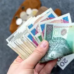 Dłoń trzyma plik polskich banknotów, w tym 100 zł. Zastanawiasz się, ile wynosi renta chorobowa?