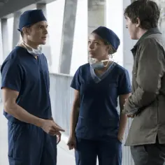 Trzech lekarzy w granatowych uniformach rozmawia na korytarzu szpitalnym. Jeden z nich, w brązowej kurtce, wydaje się być pacjentem. To scena z serialu "the good doctor".
