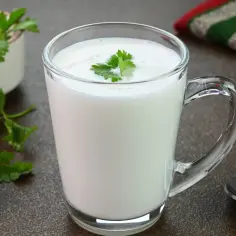 Szklanka pełna białego napoju, ozdobiona listkiem pietruszki. Zastanawiasz się, czym się różni kefir od maślanki?