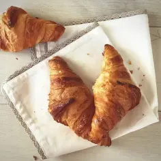 Dwa chrupiące rogaliki z ciasta francuskiego na białej serwetce. Idealne na śniadanie, sprawdzam ciasto francuskie cenę.