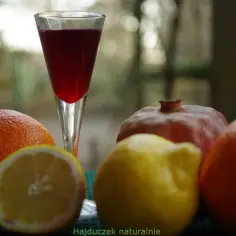 Szklaneczka z syropem z granatu, obok pomarańcze, cytryna i granat. Naturalne składniki dla zdrowia.