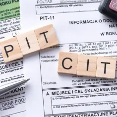 Formularze PIT i CIT, drewniane klocki z literami "PIT" i "CIT" oraz kalkulator. Temat: podatek od sprzedaży nieruchomości po upływie 5 lat.