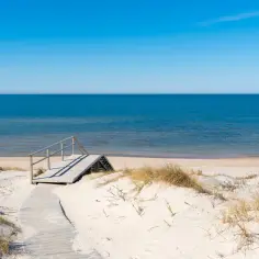Drewniane schody prowadzą na piaszczystą stegna plaża. Błękitne morze i niebo tworzą spokojny krajobraz.