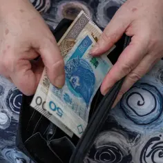 Dłonie wkładają polskie banknoty (50 zł i 200 zł) do czarnego portfela.